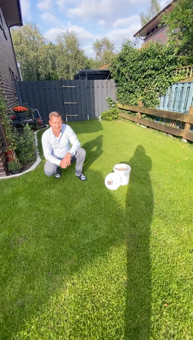 Mann kniet im Garten neben zwei Eimern turbogrün auf saftig grünem Rasen
